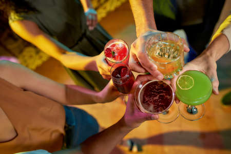 Raise your glass. Top view of group of friends, young adults, men and women having fun while...