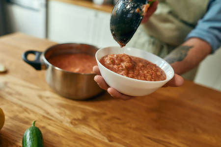 Close up of man pouring tasty soup from pot into bowl. Italian cook preparing traditional meal in the kitchen. Cooking at home, Italian cuisineの写真素材