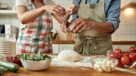 Cropped shot of couple preparing the dough together. Young man and woman in apron cooking, making pizza at home. Hobby, lifestyleの写真素材