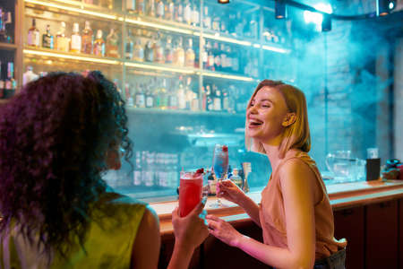 Moments of Happiness. Two women having fun, drinking cocktails while sitting at the bar counter....