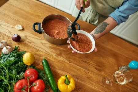 Close up of hands of man pouring tasty soup from pot into bowl. Italian cook preparing traditional meal in the kitchen. Cooking at home, Italian cuisineの写真素材