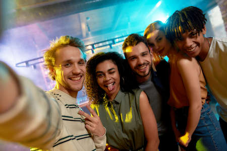 Join your friends. Close up shot of young men and women smiling while taking selfie. Multiracial...