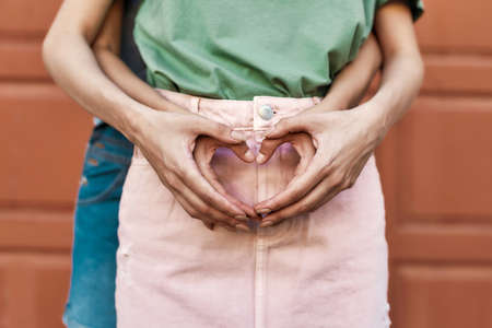 Close up of hands of young female couple making heart love sign, standing together in front of the door outdoorsの写真素材