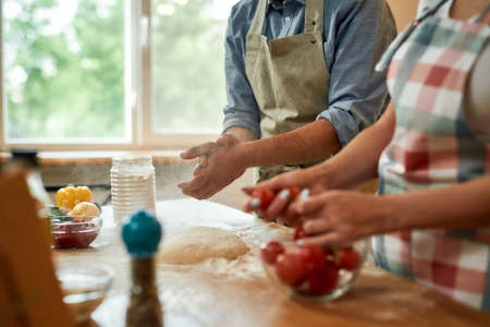 Cropped shot of couple making pizza together. Young man in apron making the dough while woman...