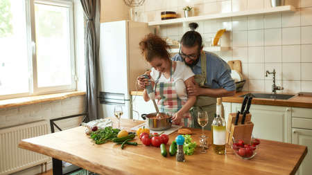 Young couple preparing a meal together in the kitchen. Italian man, chef cook helping his girlfriend to use hand blender. Cooking at home, Italian cuisineの写真素材