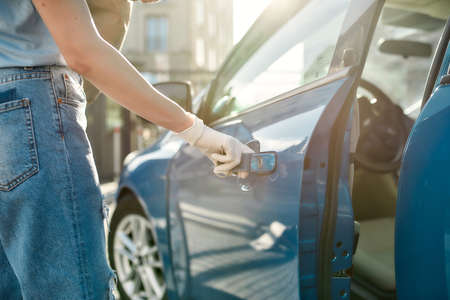 Close up of hand of woman in protective glove opening the blue car door, Protective measures against bacteria, viruses, coronavirus pandemicの写真素材