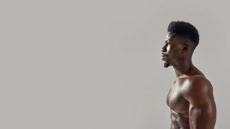 Young muscular african american man with naked torso looking away while posing shirtless isolated...