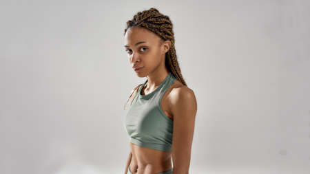 Portrait of a young attractive mixed race fitness woman in sportswear looking at camera, posing isolated over grey backgroundの写真素材