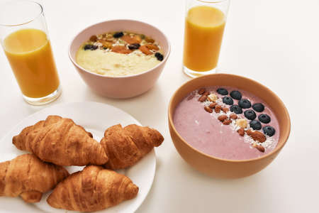 Close up of smoothie bowl with fresh berries, orange juice in glass and croissants on a plate isolated over white backgroundの写真素材