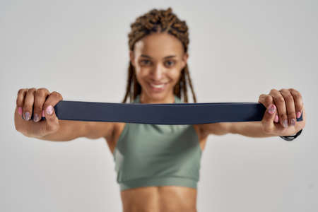 Exercising with fitness gum. Young mixed race woman in sportswear holding elastic band, looking at...