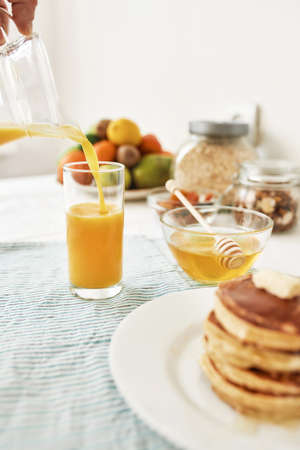 The process of pouring orange juice in the glass, Honey in a bowl with dipper, pancakes and various...