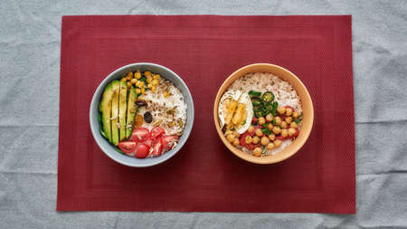 Top view of two bowls with sliced vegetables and rice served on napkin