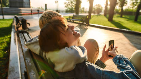 Close up of two girls having fun, sitting on the bench in the city park. Lesbian couple going to...