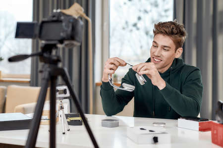 Young male technology blogger recording video blog or vlog review of new headphones and other gadgets at home studio. Blogging, Work from Home conceptの写真素材