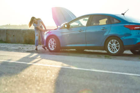 Full length shot of young woman trying to repair her broken car with open hood on her own while waiting for assistance on the road sideの写真素材