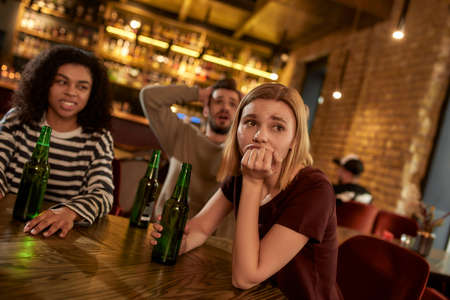 Friends looking disappointed while watching sports match on TV together, drinking beer and cheering for team in the bar. People, leisure, friendship and entertainment conceptの写真素材
