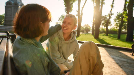 Two young women having fun, talking while sitting on the bench in the city park. Lesbian couple...