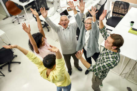 Group of diverse employees raising hands in the air, hoping for success on their plans while...