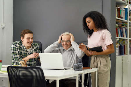 Too much information, Aged man senior intern touching head with hands while listening to his young...