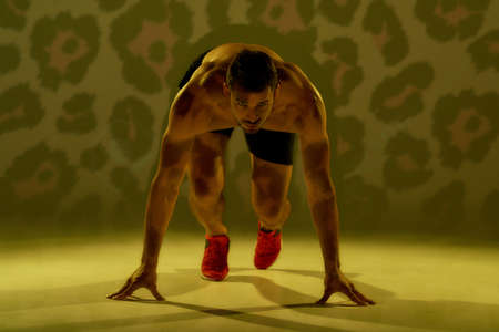Ready for run. Young muscular man standing in start position isolated over yellow cheetah...