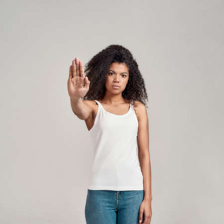 Portrait of young african american woman with curly hair wearing white shirt having serious...
