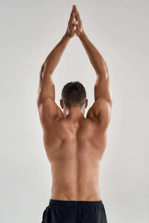 Rear view of athletic man with naked torso standing with his hands joined above his head isolated over grey backgroundの写真素材
