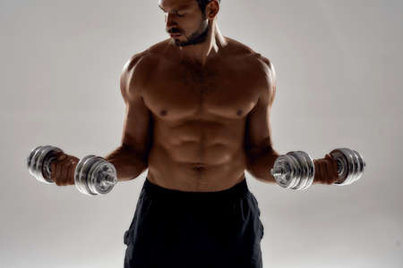 Training arms. Strong muscular caucasian man lifting weights while standing isolated over grey backgroundの写真素材
