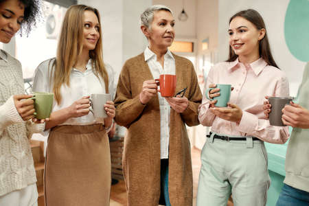 Five well-dressed women of different age having a morning coffee break during a brainstormの写真素材