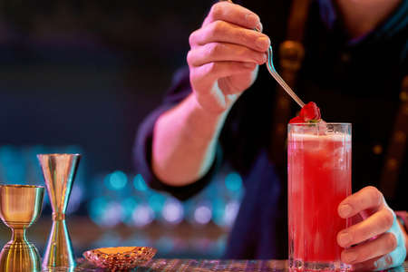 Get a drink. Close up of bartender hand decorating cocktail in glass with rose flower while making alcoholic drink at the bar counter in the night clubの写真素材