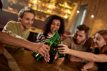 Cheers. A group of happy friends in the bar watching sports match on TV together, drinking beer, clinking bottles and cheering for team. People, leisure, friendship and entertainment conceptの写真素材