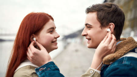 Close up of couple of teenagers going to listen to music using the same pair of earphones, looking...