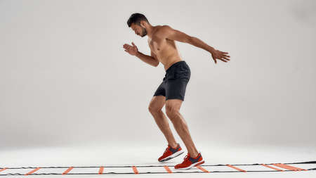 Never stop. Full length shot of young athletic man training on agility ladder drill isolated over...