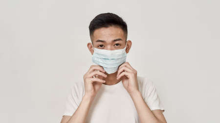 Portrait of young asian man with problematic skin wearing medical mask isolated over white background. Health care, prevention, safety conceptの写真素材