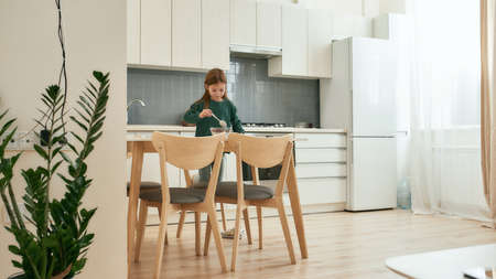 A little girl stirring her quick breakfast standing on a stoll on her knees in a big bright kitchenの写真素材