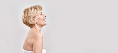 Portrait of beautiful middle aged woman in white bra looking happy, laughing while posing isolated against grey background. Beauty conceptの写真素材