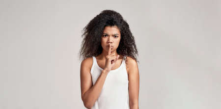 Portrait of young african american woman looking angry, making silent gesture, holding finger on her...