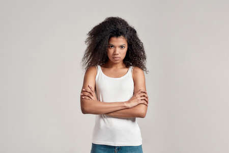 Portrait of young african american woman with curly hair wearing white shirt looking focused at...