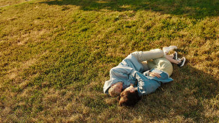 Happy young lesbian couple cuddling while lying on the grass in summer park. Womenin love looking at...