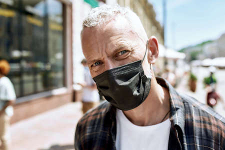 Close up portrait of middle aged man wearing mask looking at camera. People collecting their orders from the pickup point during coronavirus lockdown in the backgroundの写真素材