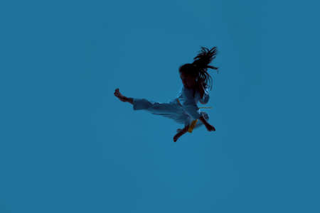 Silhouetted shot of little karate girl in white kimono exercising and fighting, doing martial arts,...