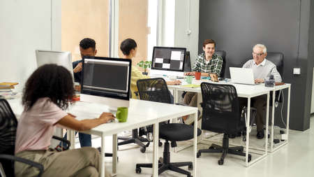 Full length shot of aged man, senior intern typing, using laptop while sitting at desk, working...