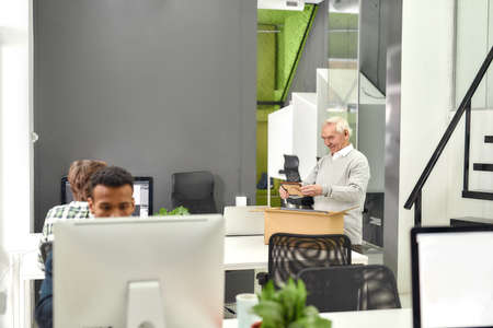 New employee aged man, senior intern looking at family picture while pulling personal belongings out...