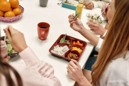 A close up of a healthy food consisting of vegetables and rice eating by a young woman sitting at a table during a business lunchの写真素材