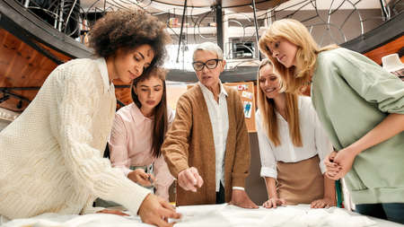A group of women of different age and nationalities speaking together and standing around a table during a brainstormの写真素材
