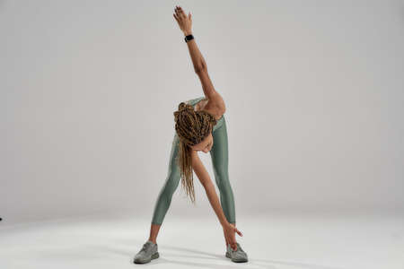 Stretching before workout. Young mixed race fitness woman in sportswear warming up while standing...
