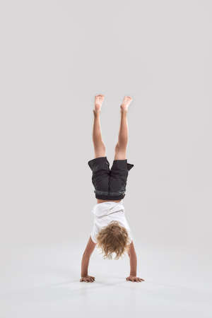 Full length shot of little playful boy child standing on his arms with legs pointing upwards...