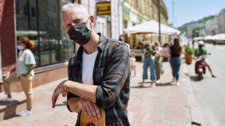 Portrait of middle aged man wearing mask holding a longboard and looking at camera. People collecting their orders from the pickup point during coronavirus lockdown in the backgroundの写真素材