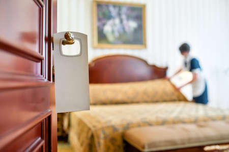 Outstanding Service. A housemaid in uniform cleaning a hotel room in the background and door with a sign at the front.の写真素材