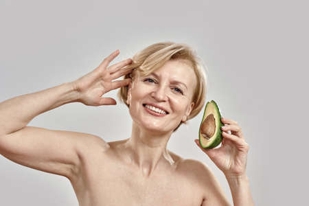 Portait of beautiful middle aged woman smiling at camera while holding half of a ripe delicious...