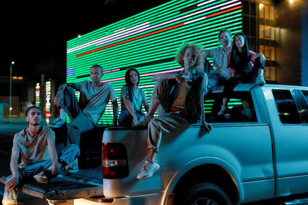 Six casually dressed youngsters of different nationalities sitting in an opened pick-ups trunk next...